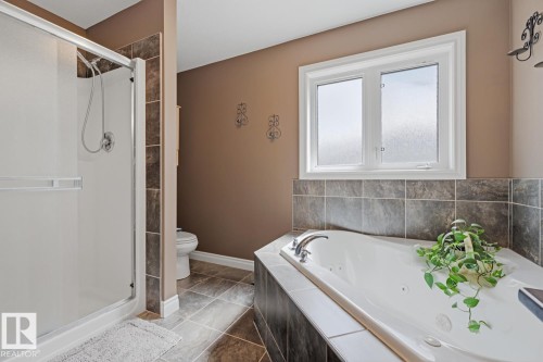 Spacious bathroom featuring an enclosed shower with sliding glass door, a separate jetted soaking tub with tiled surround, and a frosted window - 9 Danfield Place, Spruce Grove, AB - Indoor Photo Showing Bathroom