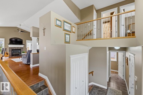 Multi-level interior featuring wood-finish flooring, a tiled fireplace with a mantel, vaulted ceilings, a ceiling fan, and a wood railing with metal spindles - 9 Danfield Place, Spruce Grove, AB - Indoor Photo Showing Other Room With Fireplace