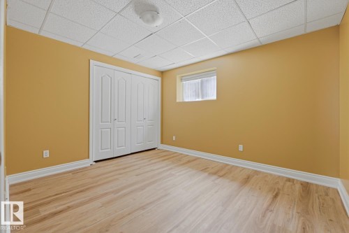Interior room featuring wood-finish flooring, warm-toned walls, white baseboards, and a bi-fold closet with panel details - 9 Danfield Place, Spruce Grove, AB - Indoor Photo Showing Other Room