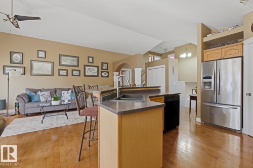 Open-concept living space featuring wood-finish flooring, a kitchen island with integrated sink, stainless steel French door refrigerator, and recessed lighting - 9 Danfield Place, Spruce Grove, AB - Indoor Photo Showing Kitchen With Double Sink
