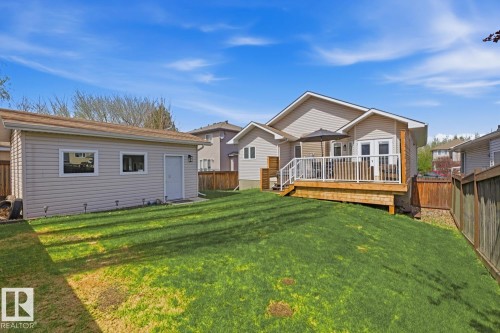 Expansive rear yard featuring a detached auxiliary structure, a raised wooden deck with white railing, and a private wooden fence - 9 Danfield Place, Spruce Grove, AB - Outdoor With Deck Patio Veranda