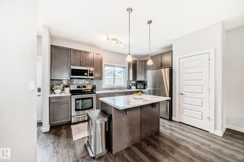 Kitchen featuring a central island with a light-toned countertop, stainless steel appliances, wood-finish flooring, recessed lighting, and pendant fixtures - 6919 Cardinal Wynd, Edmonton, AB - Indoor Photo Showing Kitchen With Stainless Steel Kitchen