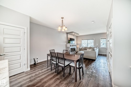 Open concept living area featuring wood-finish flooring, a dining area with a chandelier, and a living room with multiple windows and a built-in fireplace hearth - 6919 Cardinal Wynd, Edmonton, AB - Indoor Photo Showing Dining Room