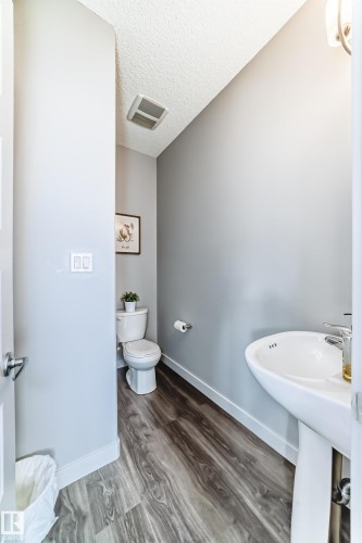 Powder room featuring a pedestal sink, a toilet, wood-finish flooring, light gray walls, and white baseboards - 6919 Cardinal Wynd, Edmonton, AB - Indoor Photo Showing Bathroom