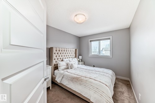 Bedroom featuring light gray walls, plush carpet flooring, a white trim window, a ceiling-mounted light fixture, and a paneled white door - 6919 Cardinal Wynd, Edmonton, AB - Indoor Photo Showing Bedroom