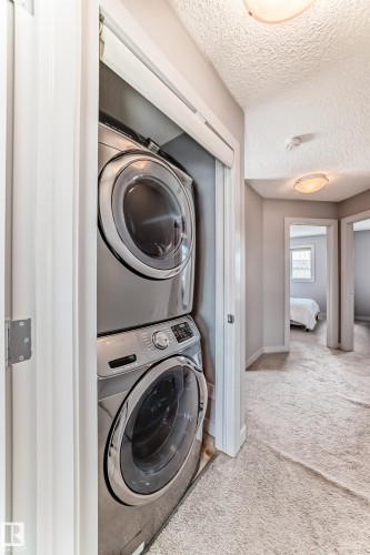 Stacked laundry appliances within a dedicated closet, featuring a front-loading washer and dryer - 6919 Cardinal Wynd, Edmonton, AB - Indoor Photo Showing Laundry Room