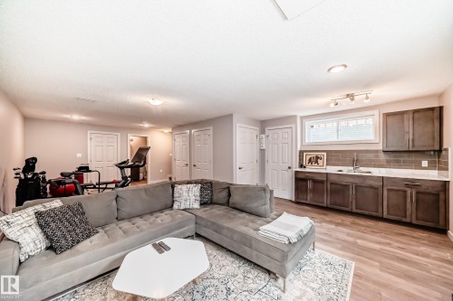 Expansive recreation room featuring wood-finish flooring, recessed lighting, and a wet bar with dark wood cabinetry, a subway tile backsplash, and a stainless steel sink - 6919 Cardinal Wynd, Edmonton, AB - Indoor Photo Showing Living Room