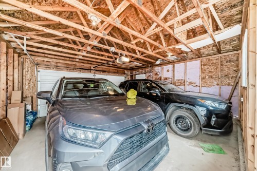 Spacious garage accommodating two SUV vehicles, featuring exposed wood rafters, a white roll-up garage door, and ample wall space - 6919 Cardinal Wynd, Edmonton, AB - Indoor Photo Showing Garage
