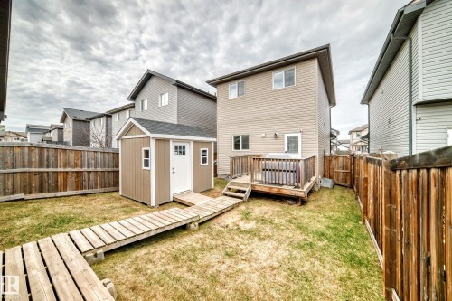 Fenced backyard featuring a raised wooden deck, 2 detached storage shed, a wooden pathway, and a grassy area - 6919 Cardinal Wynd, Edmonton, AB - Outdoor With Deck Patio Veranda With Exterior