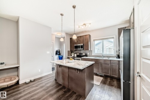 Kitchen featuring a central island, wood-finish flooring, stainless steel appliances, and wood cabinetry - 6919 Cardinal Wynd, Edmonton, AB - Indoor Photo Showing Kitchen