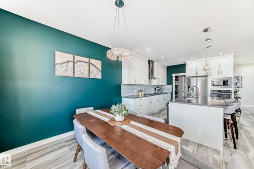 Open-concept dining area featuring a dark teal accent wall, wood-finish flooring, and a contemporary chandelier - 3716 46 Avenue, Beaumont, AB - Indoor