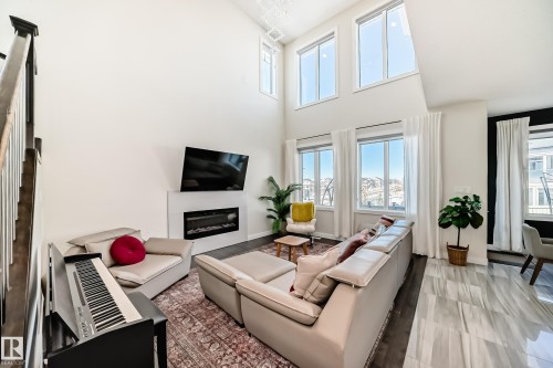 Soaring ceilings with upper-level windows complement the expansive lower windows, providing abundant natural light - 3716 46 Avenue, Beaumont, AB - Indoor Photo Showing Living Room With Fireplace