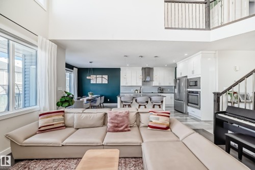 Open-concept living space featuring high ceilings, large windows, a modern kitchen with stainless steel appliances, a kitchen island with seating, and a formal dining area with a statement wall - 3716 46 Avenue, Beaumont, AB - Indoor Photo Showing Living Room