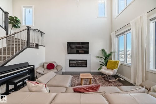 Two-story living area featuring a modern electric fireplace, large windows with white trim, and dark wood-finish flooring - 3716 46 Avenue, Beaumont, AB - Indoor With Fireplace