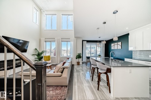 Open-concept living space featuring high ceilings, large windows, wood-finish flooring, a contemporary kitchen island with seating, and a sleek fireplace - 3716 46 Avenue, Beaumont, AB - Indoor