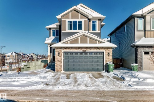 Two-story residential exterior featuring a stone and siding facade, a double-car garage with paneling, multiple windows with white trim, and a gabled roofline - 3716 46 Avenue, Beaumont, AB - Outdoor
