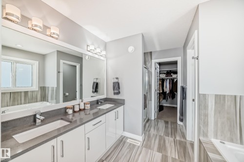 Bathroom featuring a dual-sink vanity with a dark countertop and white cabinetry, a large mirror, and contemporary lighting fixtures - 3716 46 Avenue, Beaumont, AB - Indoor Photo Showing Bathroom