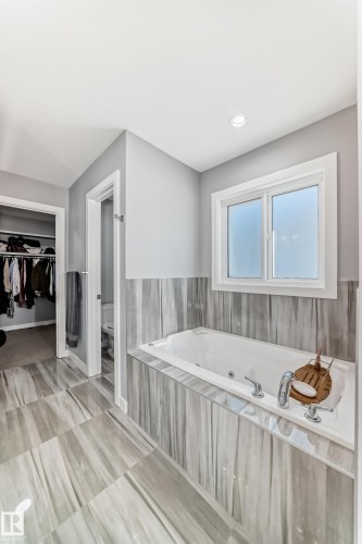 Bathroom featuring a built-in jetted tub with polished chrome fixtures, set within a tiled surround and light-toned wall paneling - 3716 46 Avenue, Beaumont, AB - Indoor Photo Showing Bathroom