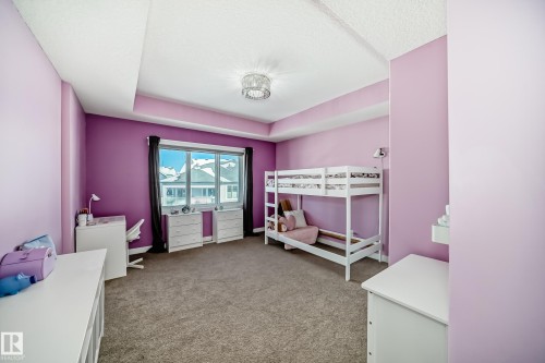 Carpeted room featuring a large window, tray ceiling, and a modern ceiling light fixture - 3716 46 Avenue, Beaumont, AB - Indoor Photo Showing Bedroom