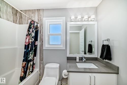 Bathroom featuring a white vanity with a gray countertop and integrated sink, a framed mirror, a four-light vanity fixture, a white toilet, and a shower-tub combination with tile surround - 3716 46 Avenue, Beaumont, AB - Indoor Photo Showing Bathroom