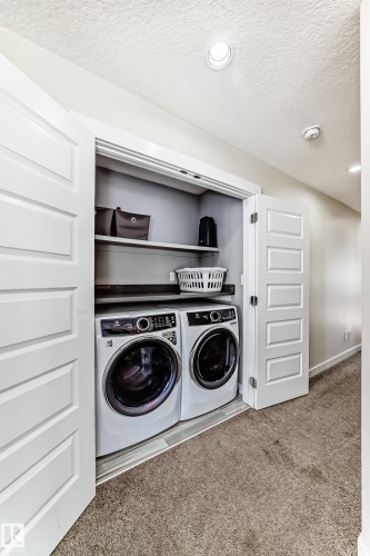 Dedicated laundry area featuring a front-loading washer and dryer set, built-in shelving, and bifold panel doors - 3716 46 Avenue, Beaumont, AB - Indoor Photo Showing Laundry Room