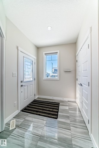 Entryway featuring wide plank tile flooring with a grey and white marble-look pattern, a white paneled front door with decorative glass inserts, and a window providing natural light - 3716 46 Avenue, Beaumont, AB - Indoor Photo Showing Other Room