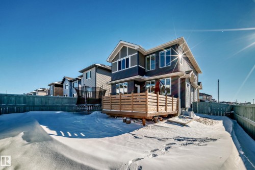 Rear exterior featuring dark gray siding, a light wood-toned deck with slatted railing, and multiple large windows - 3716 46 Avenue, Beaumont, AB - Outdoor