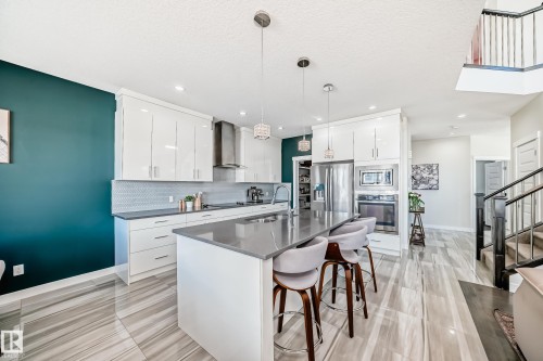 Open-concept kitchen featuring an oversized island with seating, glossy white cabinetry, stainless steel appliances, and a unique tile backsplash - 3716 46 Avenue, Beaumont, AB - Indoor Photo Showing Kitchen With Upgraded Kitchen
