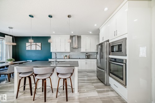 Modern kitchen featuring white cabinetry, stainless steel appliances including a built-in oven and microwave, a large kitchen island with a sink, and pendant lighting - 3716 46 Avenue, Beaumont, AB - Indoor Photo Showing Kitchen With Upgraded Kitchen