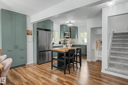 Open-concept kitchen featuring teal cabinetry, stainless steel appliances, a central island with wood countertop, and wood-finish flooring - 13316 109A Avenue, Edmonton, AB - Indoor