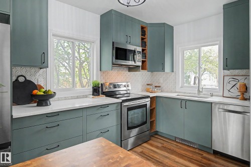 Kitchen featuring teal cabinetry with black hardware, white countertops, stainless steel appliances, and wood-finish flooring - 13316 109A Avenue, Edmonton, AB - Indoor Photo Showing Kitchen With Upgraded Kitchen