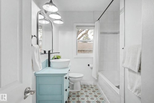 Bathroom featuring a light blue vanity with a vessel sink, patterned floor tiling, white subway tile shower surround, and a window - 13316 109A Avenue, Edmonton, AB - Indoor Photo Showing Bathroom