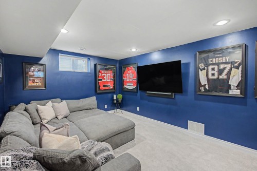 Entertainment area featuring recessed lighting, a mounted flat-screen television, blue painted walls, light gray carpet flooring, and a single window - 13316 109A Avenue, Edmonton, AB - Indoor