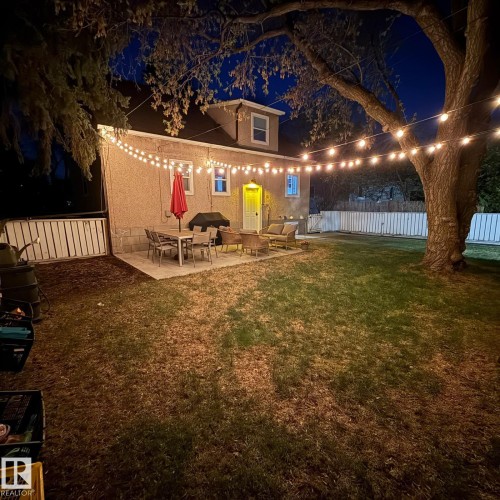 Expansive backyard featuring a concrete patio, string lighting, and a white privacy fence - 13316 109A Avenue, Edmonton, AB - Outdoor