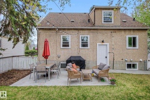 Rear exterior featuring a concrete patio, shingle roof, dormer window, lower-level windows, and a white rear entry door - 13316 109A Avenue, Edmonton, AB - Outdoor With Exterior