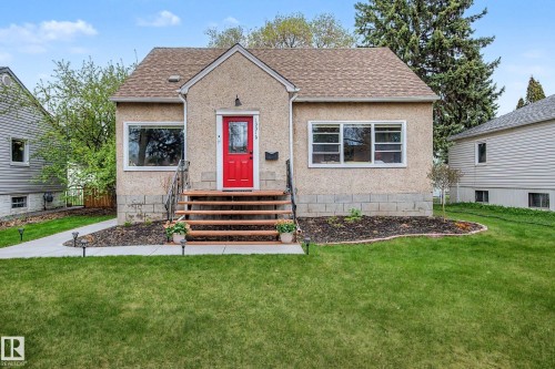 Stucco exterior featuring a prominent red entry door, natural wood steps with a metal handrail, white window frames, and a shingle roof - 13316 109A Avenue, Edmonton, AB - Outdoor