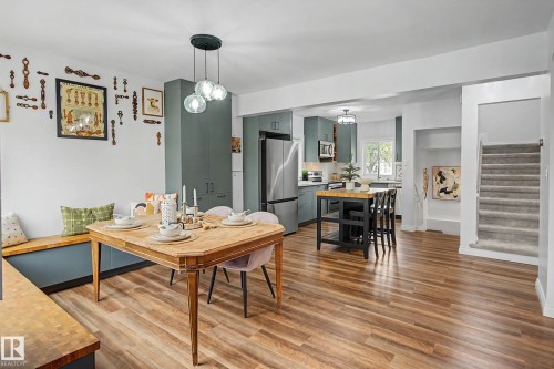 Open-concept dining area featuring wood-finish flooring, a built-in bench with a butcher block top, and a modern three-globe pendant light - 13316 109A Avenue, Edmonton, AB - Indoor Photo Showing Dining Room