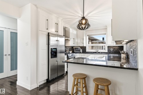 Kitchen featuring white shaker-style cabinetry, black stone countertops, and a mosaic tile backsplash - 14608 97 Avenue, Edmonton, AB - Indoor Photo Showing Kitchen