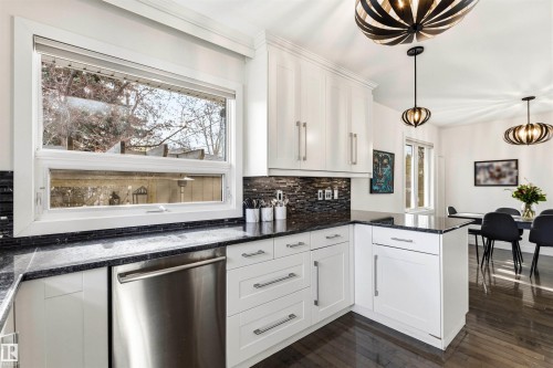 Modern kitchen featuring white cabinetry, dark stone countertops, a dark tile backsplash, stainless steel dishwasher, and wood-finish flooring - 14608 97 Avenue, Edmonton, AB - Indoor Photo Showing Kitchen