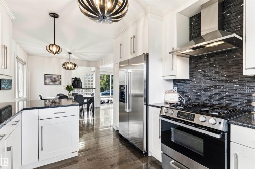 Contemporary kitchen featuring white cabinetry, dark granite countertops, a dark glass tile backsplash, stainless steel appliances, and wood-finish flooring - 14608 97 Avenue, Edmonton, AB - Indoor Photo Showing Kitchen With Stainless Steel Kitchen With Upgraded Kitchen