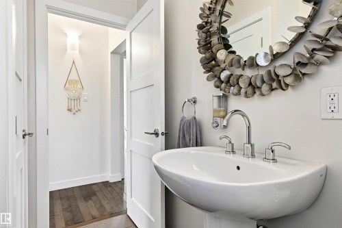 Pedestal sink with chrome fixtures and a round mirror with a unique frame - 14608 97 Avenue, Edmonton, AB - Indoor Photo Showing Bathroom