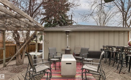 Expansive wood-decked patio featuring a slatted pergola, attached string lighting, and a contemporary fire pit - 14608 97 Avenue, Edmonton, AB - Outdoor With Deck Patio Veranda