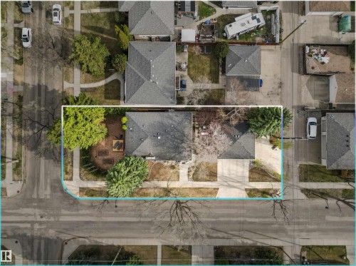 Corner lot property featuring a main residence with a dark shingle roof, a detached structure with a dark shingle roof, mature trees providing canopy, paved sidewalks, and a concrete driveway - 14608 97 Avenue, Edmonton, AB - 