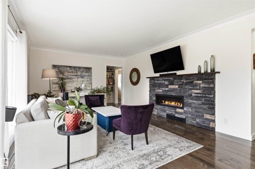 Living area featuring a floor-to-ceiling stacked stone fireplace with a built-in linear electric firebox, dark wood-finish flooring, white crown molding, and a large window with white drapery - 14608 97 Avenue, Edmonton, AB - Indoor Photo Showing Living Room With Fireplace