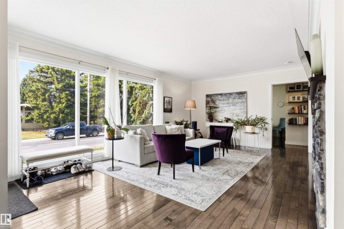 Living area featuring expansive windows, wood-finish flooring, crown molding, and a stone-clad fireplace surround with a wood mantel - 14608 97 Avenue, Edmonton, AB - Indoor Photo Showing Living Room