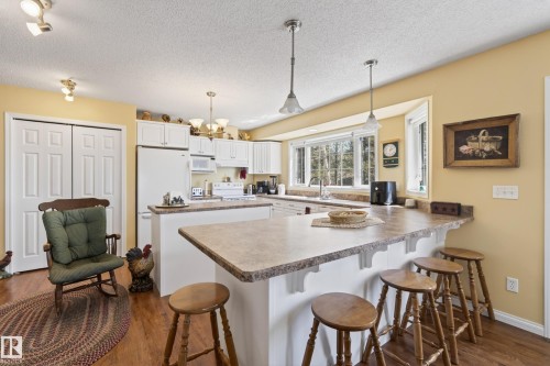 Kitchen with white cabinetry, wood-finish flooring, and a breakfast bar - 77 Lakeshore Drive, Rural Leduc County, AB - Indoor