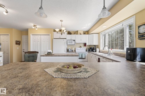 Kitchen featuring white cabinetry, a large center island with a stone-finish countertop, and a window overlooking a wooded area - 77 Lakeshore Drive, Rural Leduc County, AB - Indoor Photo Showing Kitchen