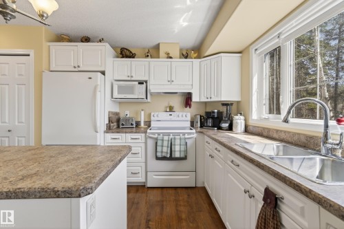 Kitchen featuring white cabinetry, wood-finish flooring, a double-basin stainless steel sink, light-toned countertops, and a window with exterior views - 77 Lakeshore Drive, Rural Leduc County, AB - Indoor Photo Showing Kitchen With Double Sink