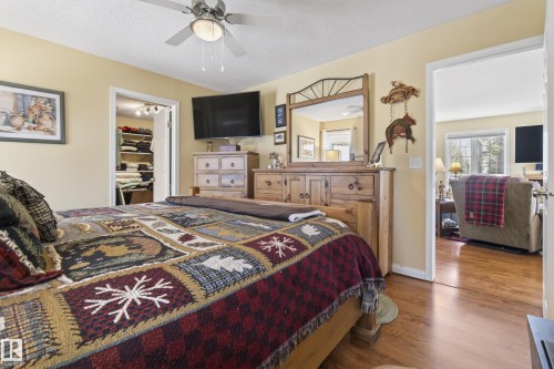 Bedroom featuring a ceiling fan with integrated lighting, a walk-in closet, and a doorway opening to an additional room with wood-finish flooring and a window - 77 Lakeshore Drive, Rural Leduc County, AB - Indoor Photo Showing Bedroom