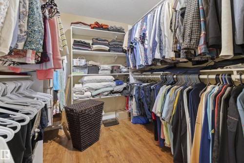 Walk-in closet featuring wood-finish flooring, white built-in shelving, and multiple clothing rods for extensive storage - 77 Lakeshore Drive, Rural Leduc County, AB - Indoor With Storage
